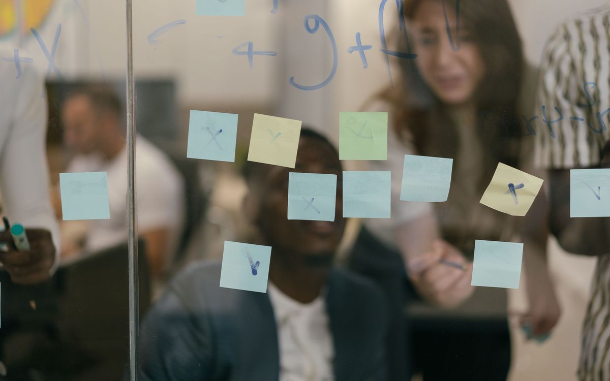Consultants and a client team mapping a process on a glass wall of sticky notes during a systems audit workshop