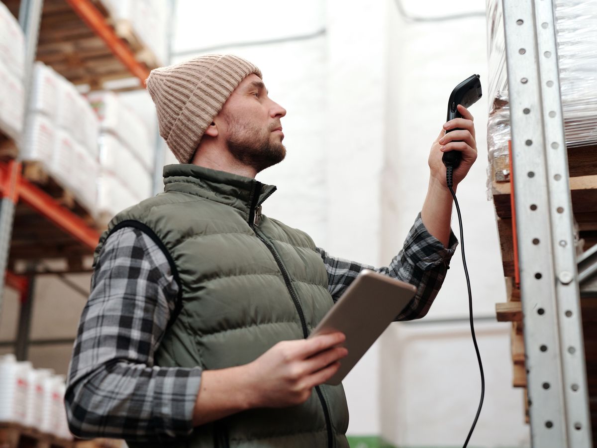 Warehouse operative scanning stock with a handheld scanner and tablet in a racking aisle